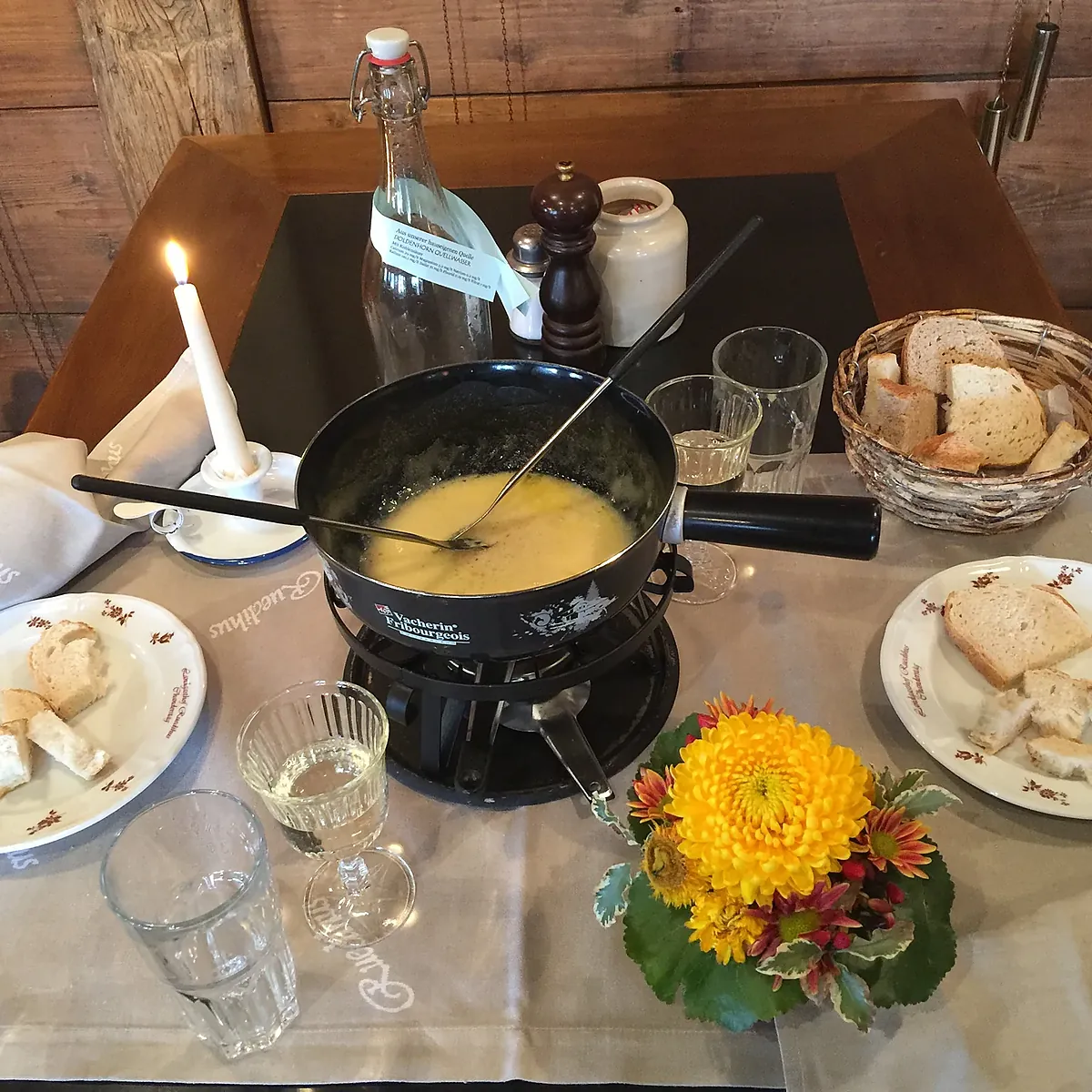 Fondue im Caquelon, Brot, Kerze und eine Herbstblume