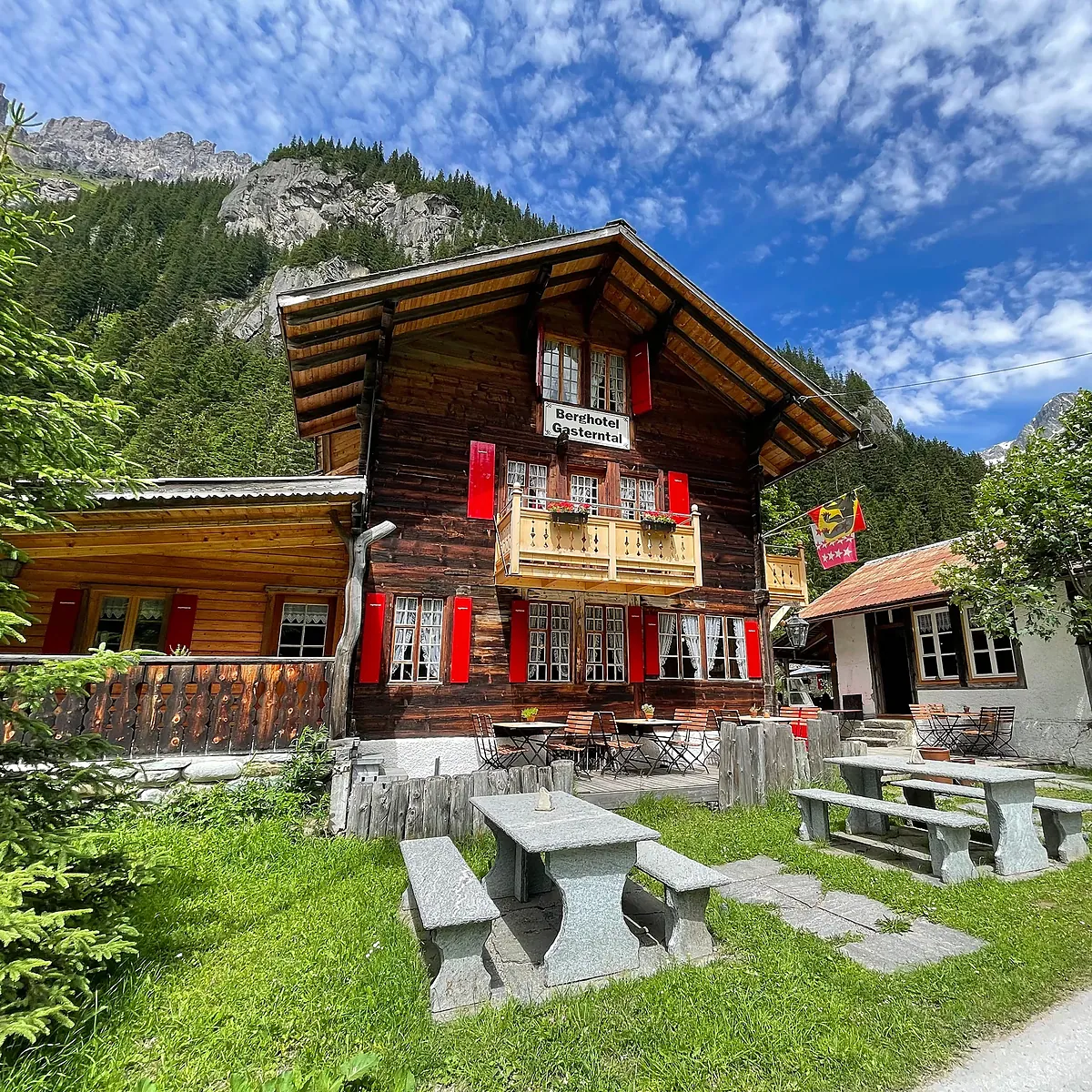 Giebelseite des Berghotels mit Balkon, Geranien und Hausschild, davor Steintische